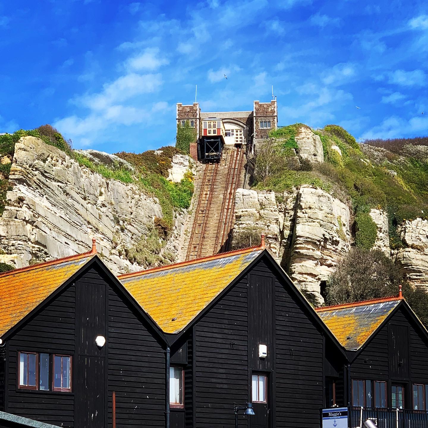 Standing on the beach amongst lobster pots, fishing boats, buoys, old rope and tarpaulin flapping gently in the breeze, looking up across the fish market to the East Hill and the funicular railway.  #hastings #easthillfunicular #fishingindustry #daysout #besidethesea #rockanorefisheries